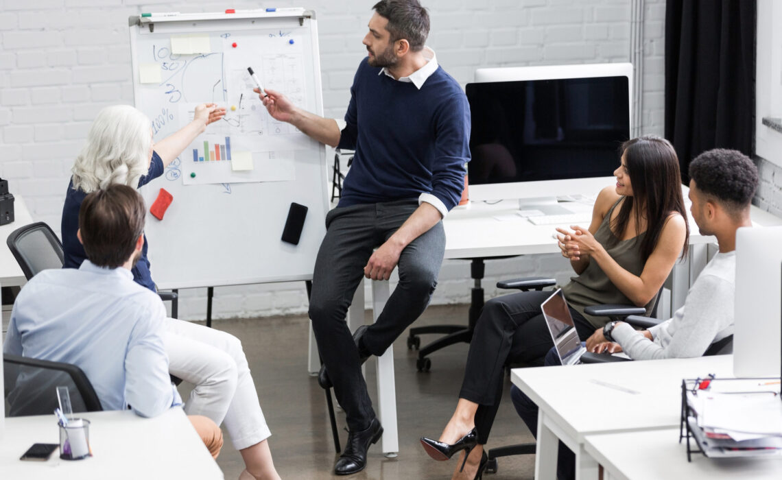 Creative people sitting at table in boardroom with man explaining business strategy